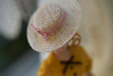 Close-up of the blush pink ribbon and bow on a beige miniature straw hat