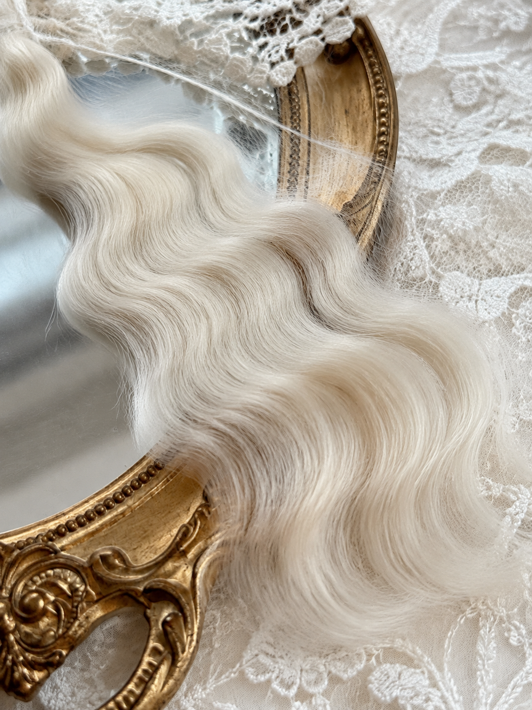 Close-up of platinum blonde natural mohair doll hair showing fine fibers, waves and silky sheen